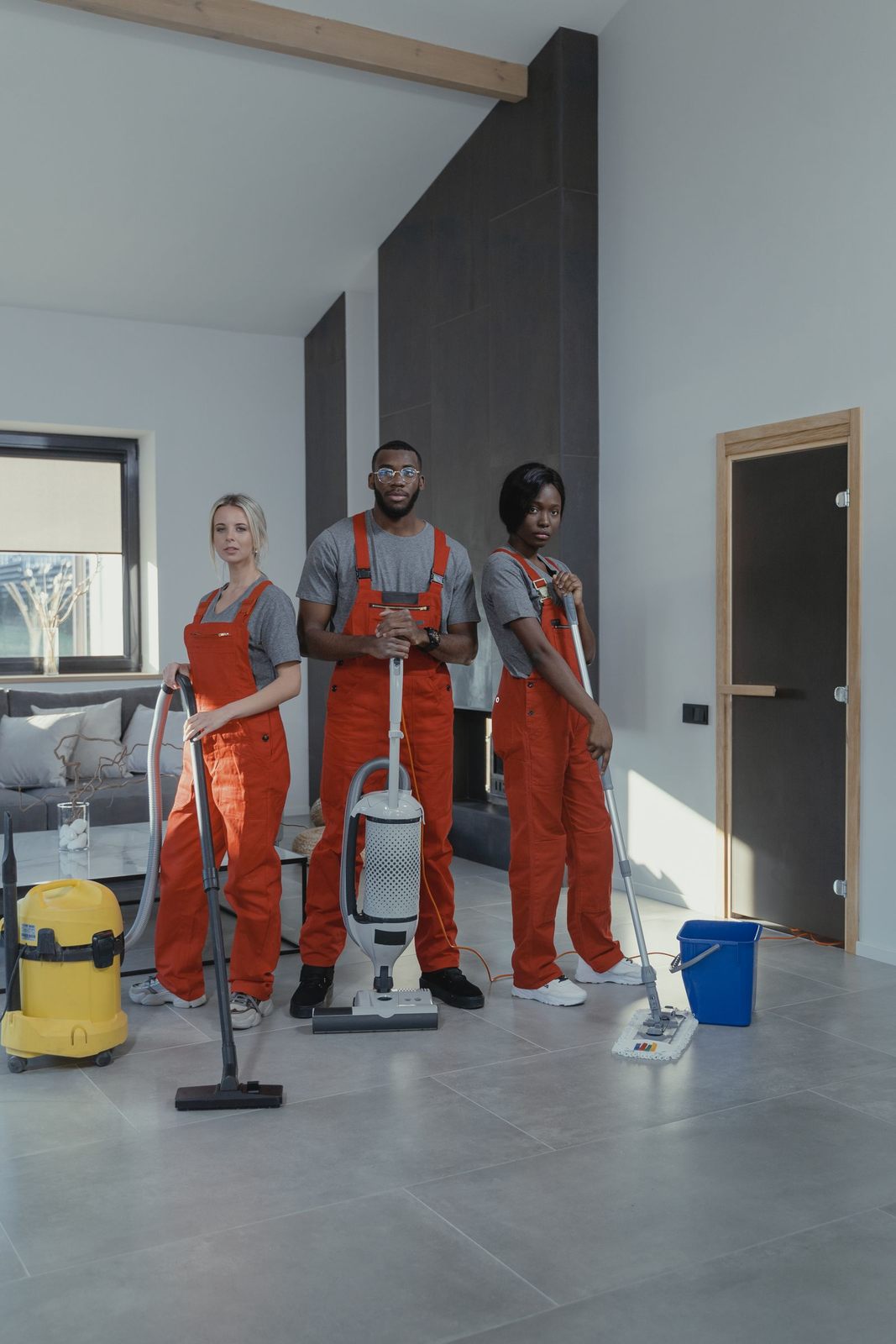 Three professional cleaners in uniform inside a modern home with cleaning equipment
