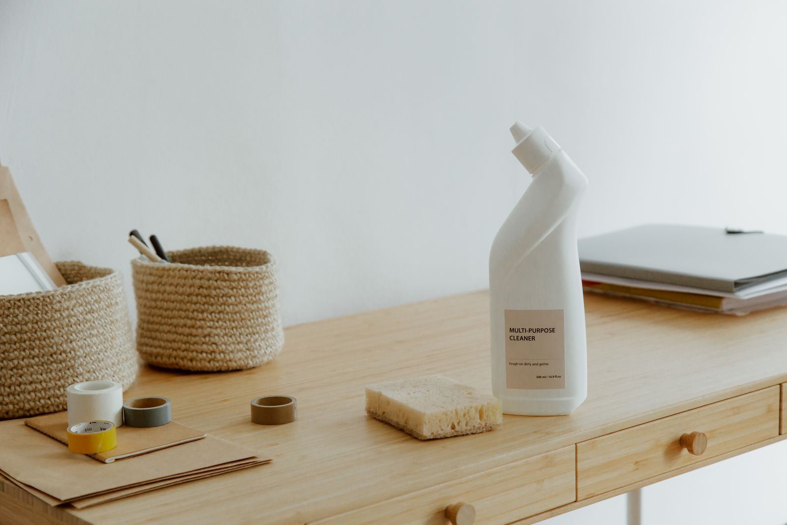 A minimalist home office desk featuring cleaning supplies and organized baskets in a neutral-toned interior